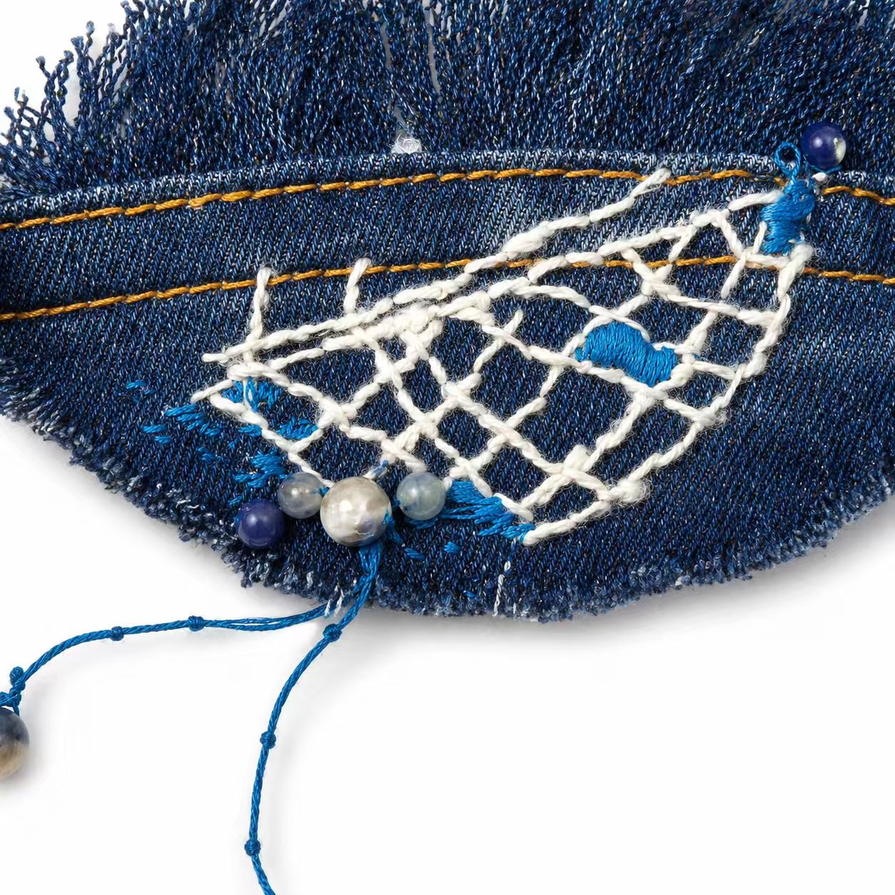 Close-up of stitched netting and beads on blue denim